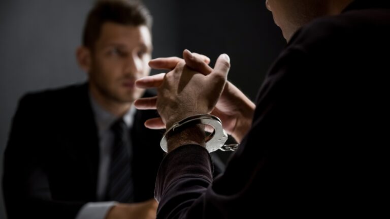 Criminal man with handcuffs being interviewed in interrogation