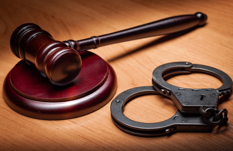 Wooden judge's gavel and steel police handcuffs on a wooden desk